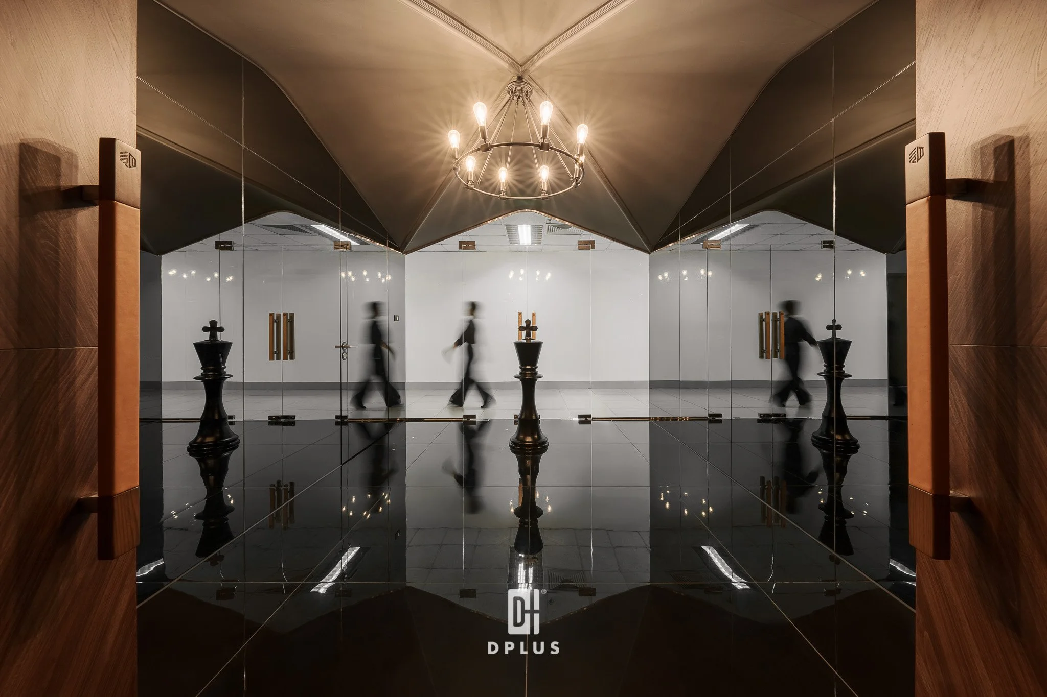 Reflection of a chandelier and people walking through a mirrored wall in a modern interior space.