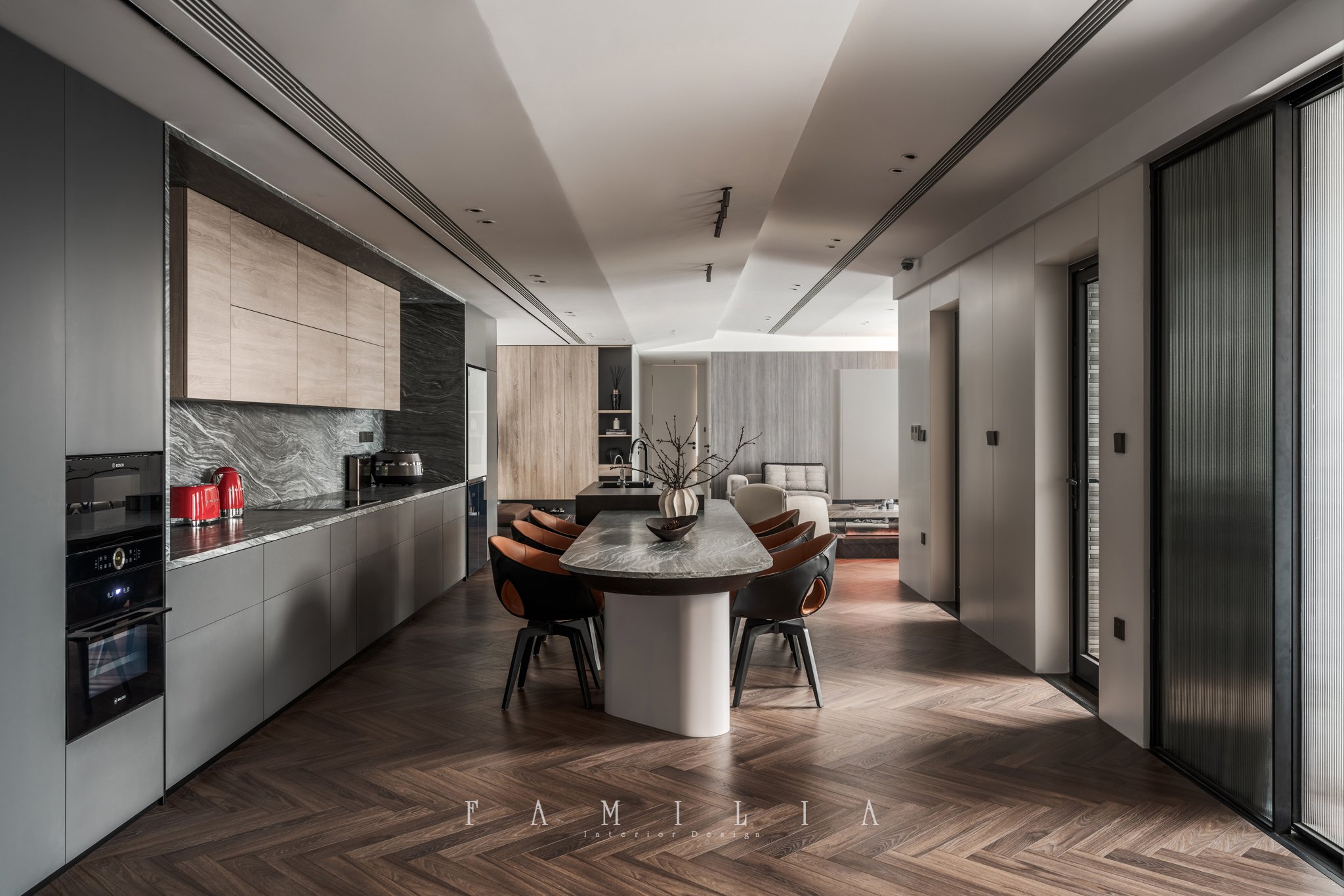Modern kitchen and living space with a marbled kitchen island, dining table with chairs, and a seating area in the background. Sleek cabinetry and large windows are visible.