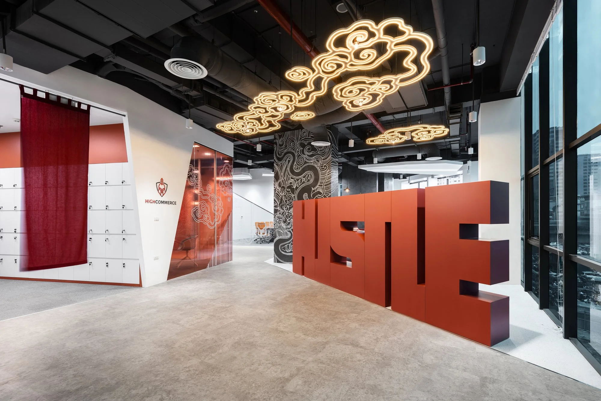 Modern office lobby with cloud-shaped neon light fixtures hanging from the ceiling, large windows, and a red and white color scheme.