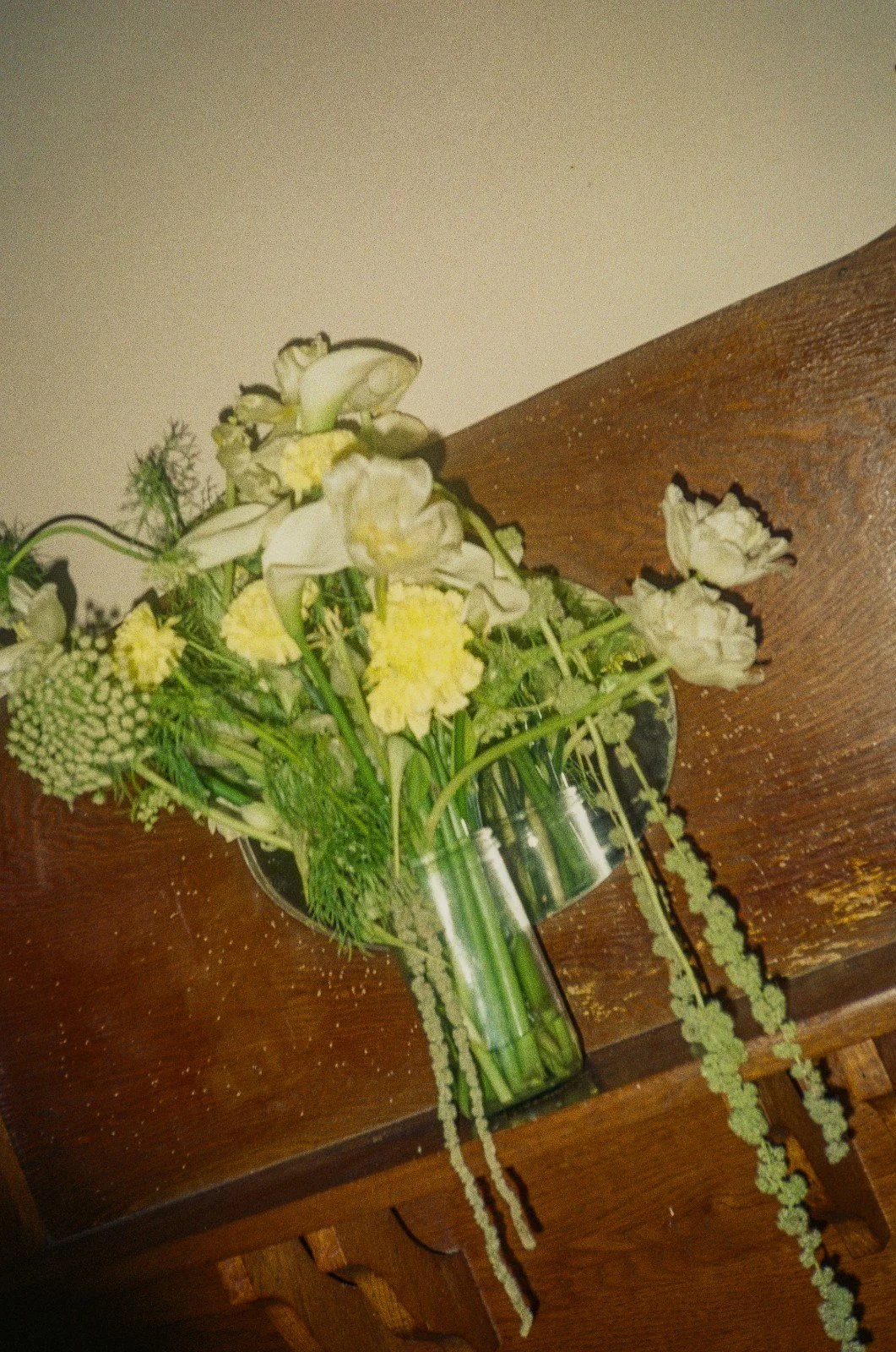 A floral arrangement with white and yellow flowers in a glass vase on a wooden surface.