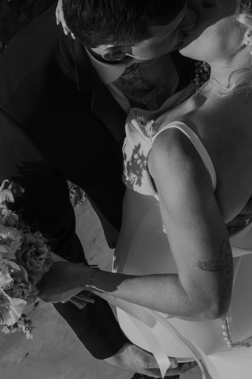 A couple sharing a kiss during a wedding ceremony, with the bride holding a bouquet of flowers and wearing a wedding dress, and the groom dressed in a suit.