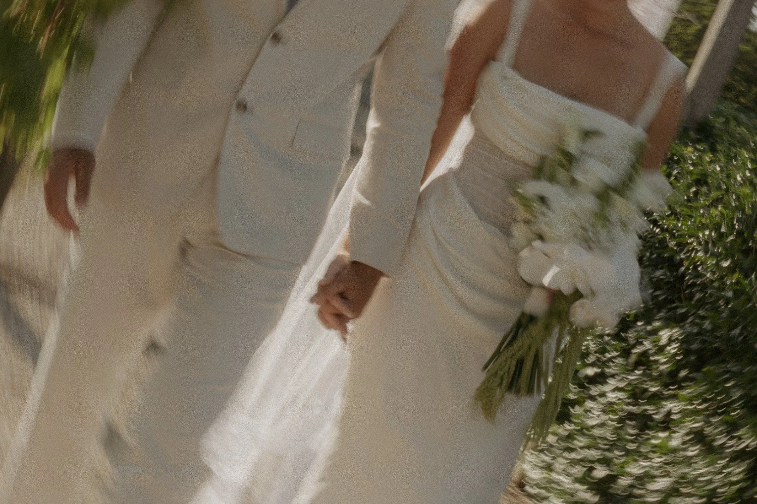 Close-up view of a bride and groom holding hands during their wedding ceremony, with the bride holding a white floral bouquet.
