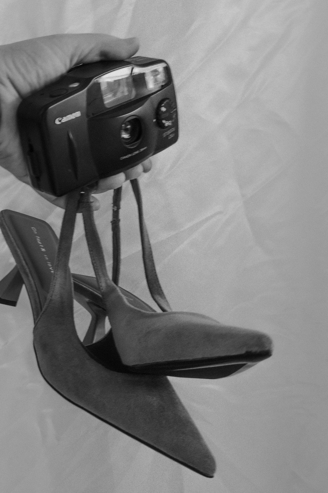 A bride holding a film camera with a strap, standing on a tiled floor.