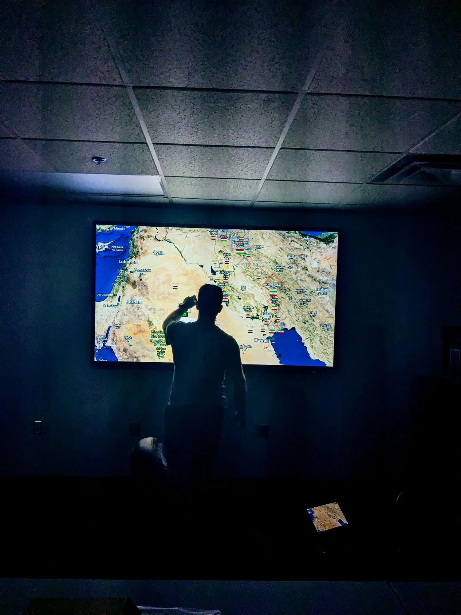 A person standing in front of a large screen displaying a map of the Middle East and surrounding regions, in a dark room.