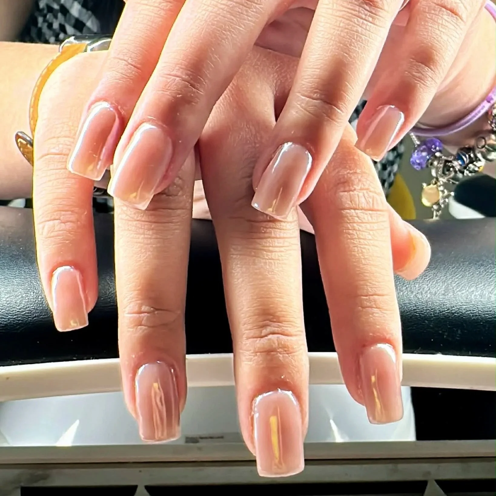 Close-up of hands with long, well-manicured nails, held over a surface with hanging jewelry and a white cup visible underneath.