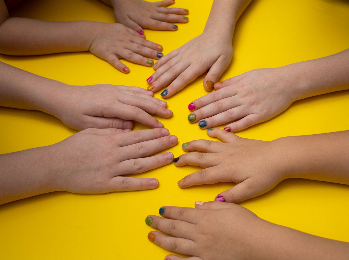 Multiple children's hands with painted nails on a yellow surface, arranged in a circle.