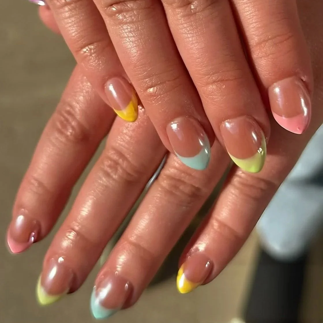 Colorful French manicured nails with pastel tips in yellow, pink, green, and blue on slightly wet, well-manicured fingers.