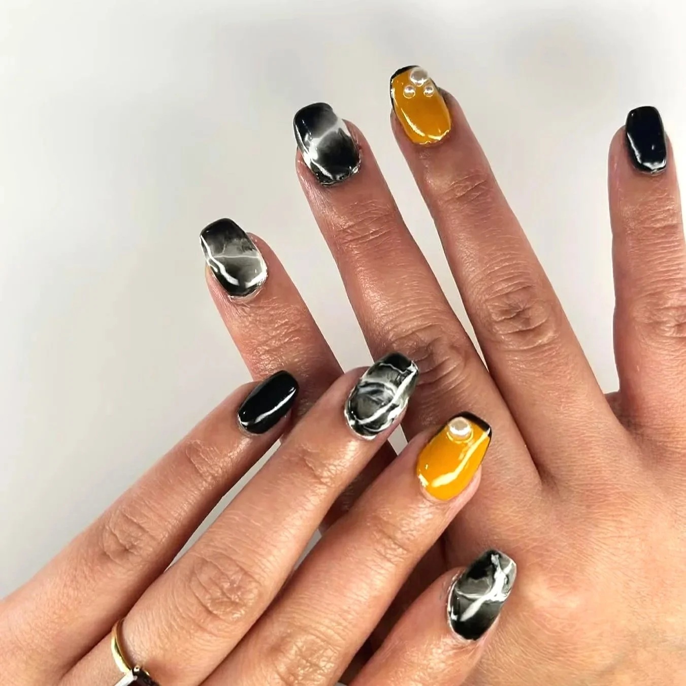 Close-up of two hands with manicured nails. One hand has black and marble pattern nails, while the other has black and yellow nails, all with a shiny finish.