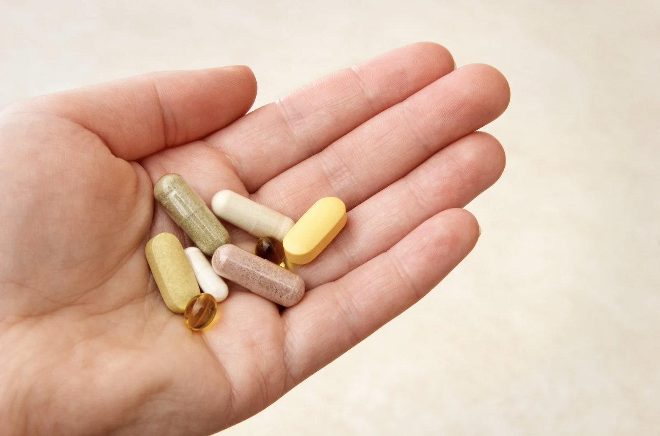 A hand holding various pills and capsules of different colors and shapes.