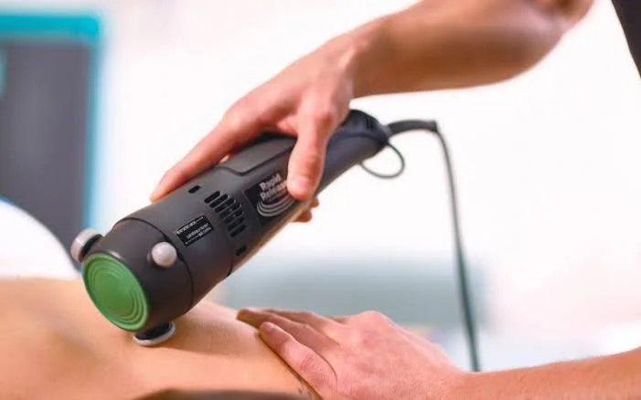 A person receiving a thermal or ultrasound treatment on their leg from a healthcare provider using a handheld device.