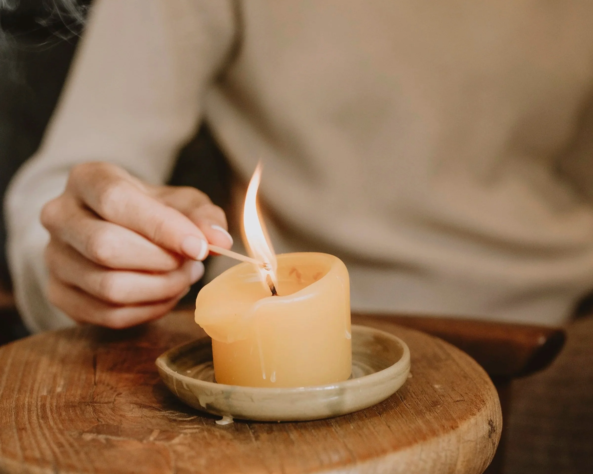 Hands lighting a yellow candle with a matchstick on a wooden surface.