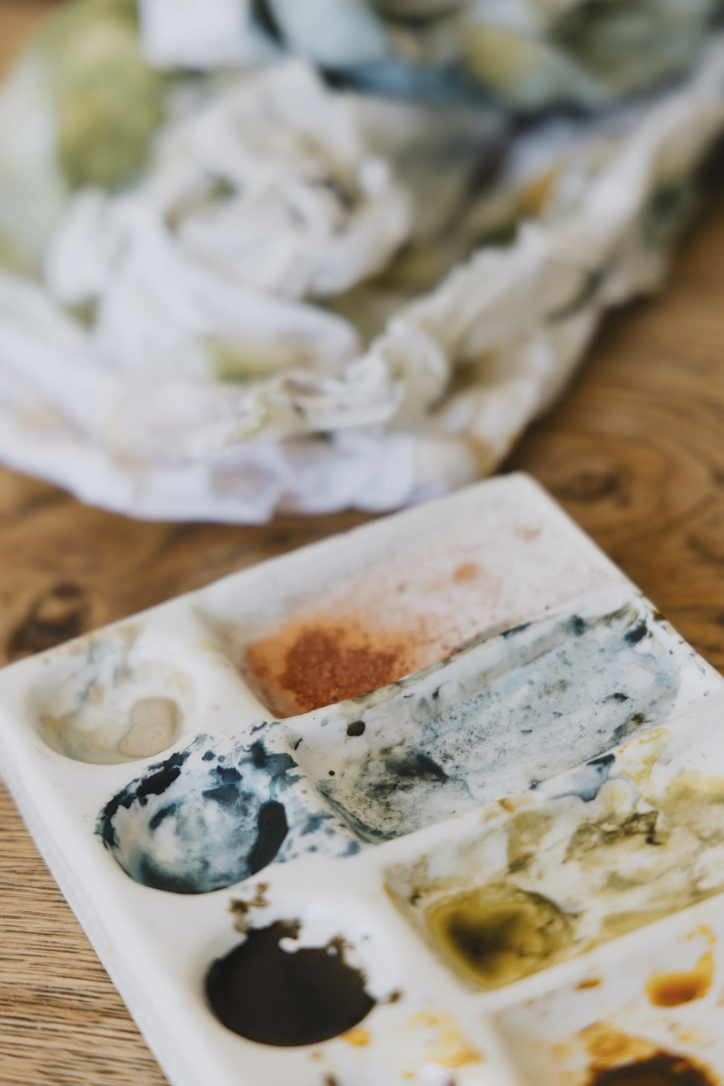 Close-up of a watercolor palette with various colors, some mixed, on a wooden surface.