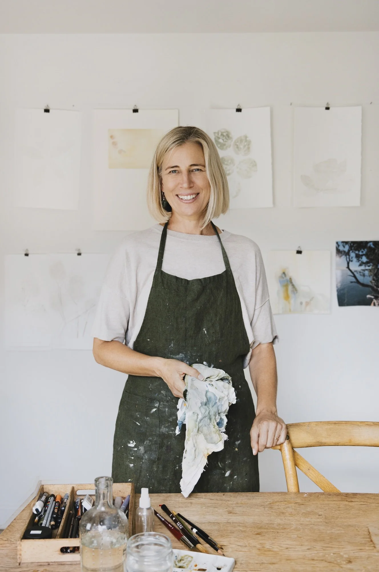 Nicky Scoltock in her Auckland art studio, wearing a paint-covered apron and standing beside her work table.