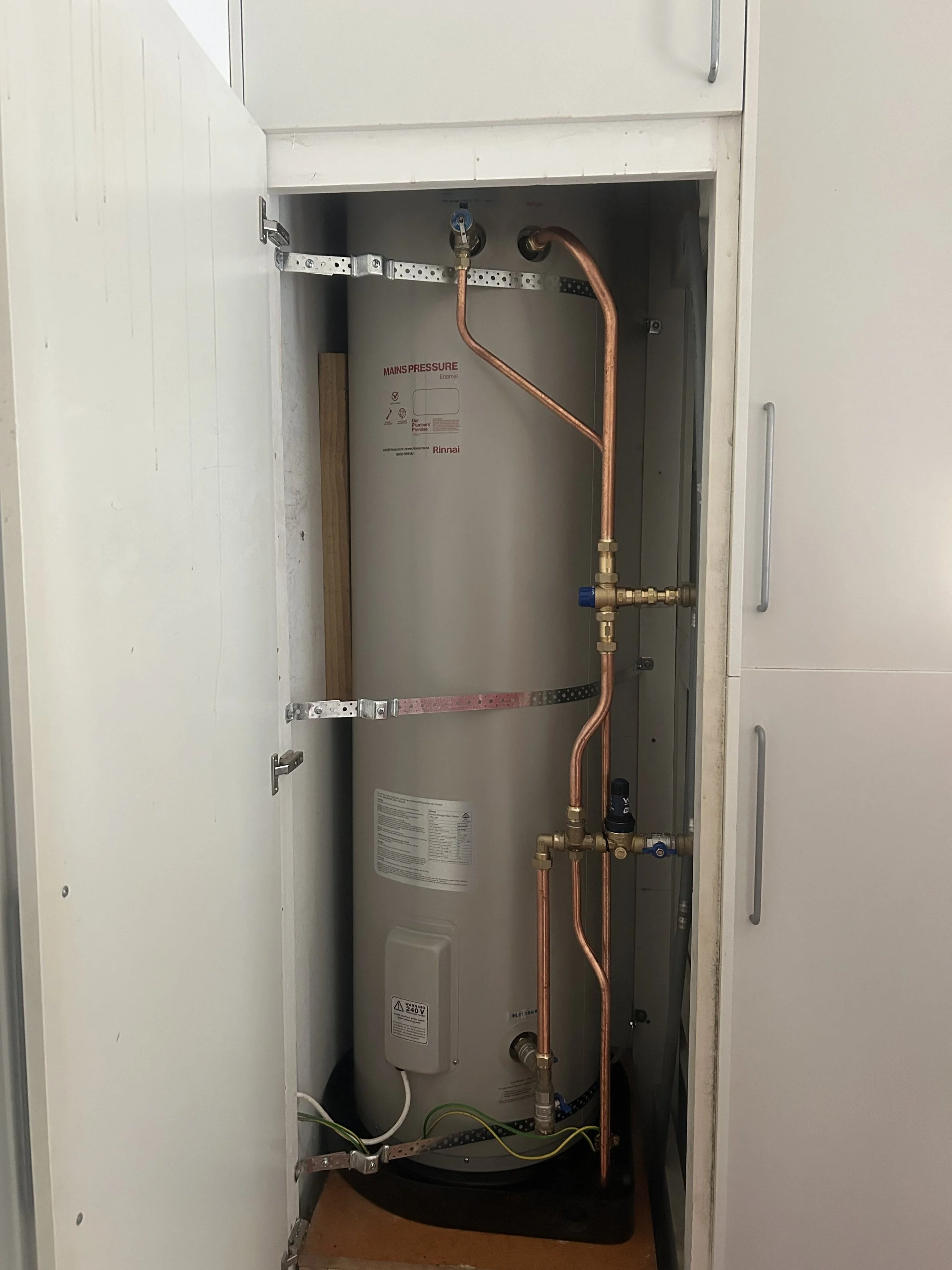 Inside a cabinet showing a water heater with copper and metal pipes connected.
