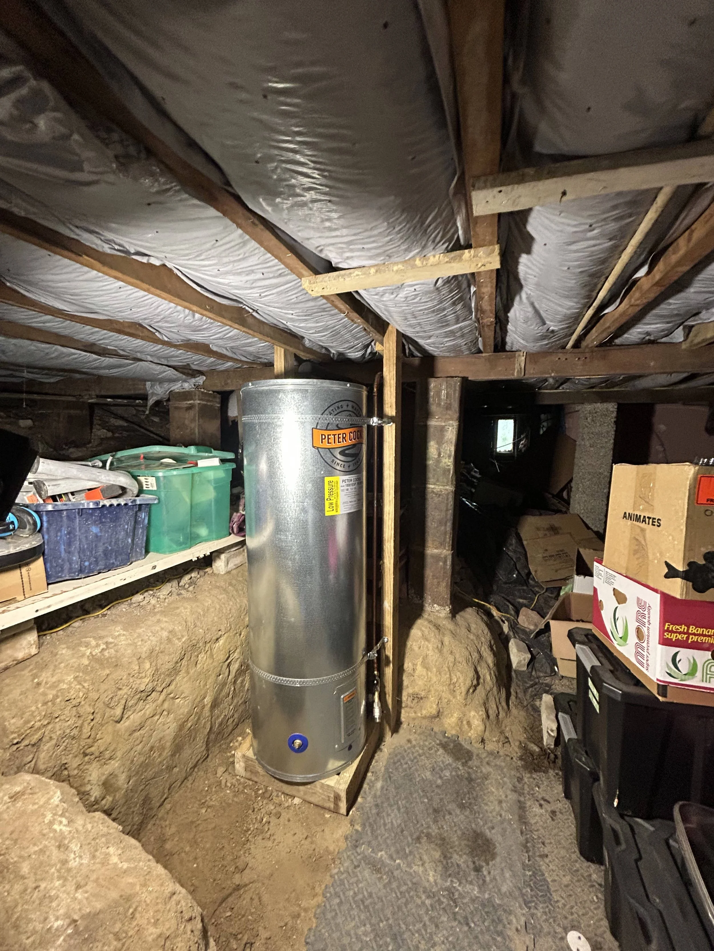 A basement space with insulation on the ceiling, storage shelves with boxes and tools, and a water heater in the center.