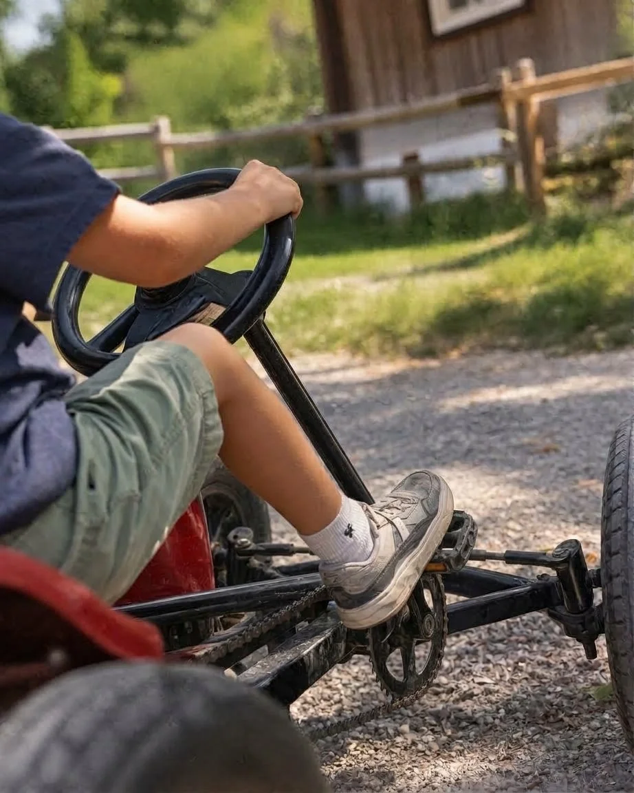 Person fährt ein Gokart auf einem Schotterweg vor einem Bauernhof.