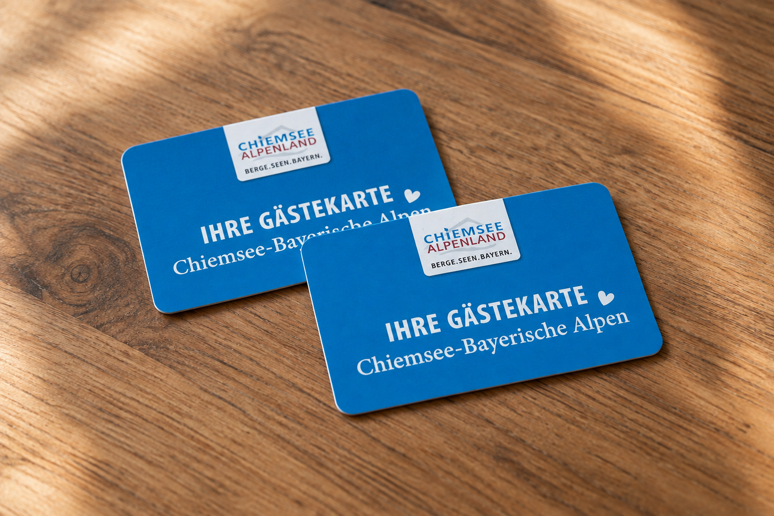 Zwei blaue Gästekarten für die Chiemsee-Bayerische Alpen liegen auf einem Holztisch.