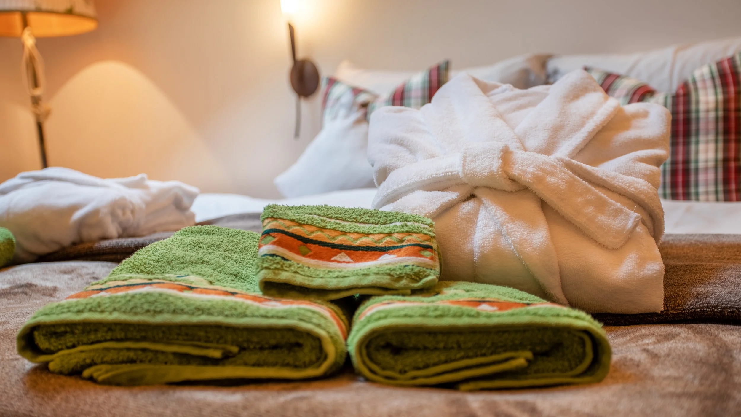 Ein aufgeräumtes Bett mit Handtüchern. Neben dem Bett steht eine Nachttischlampe an der Wand.