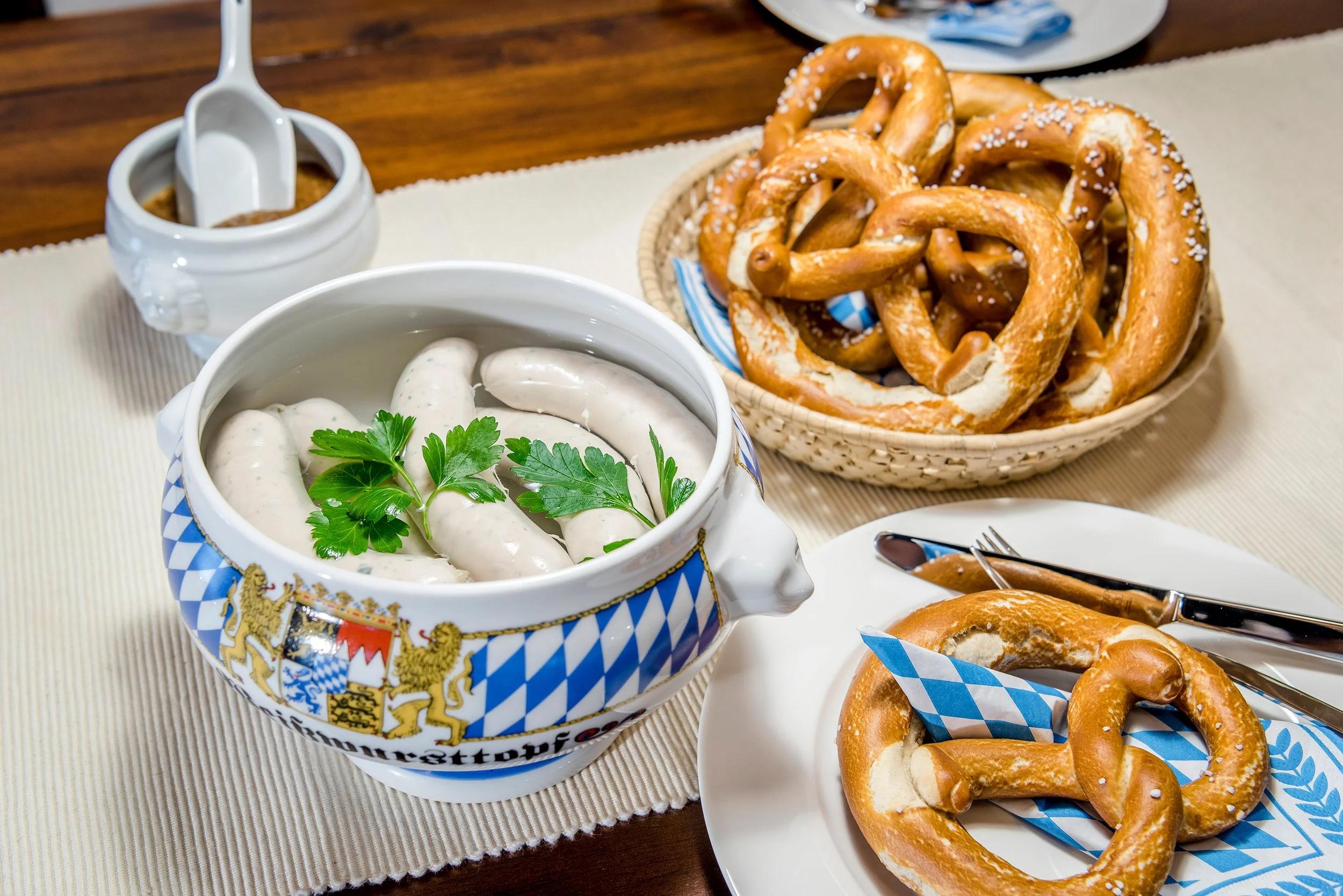 Brotzeit mit Brezeln, Weißwürsten, Senf und Petersilie auf einem Tisch.