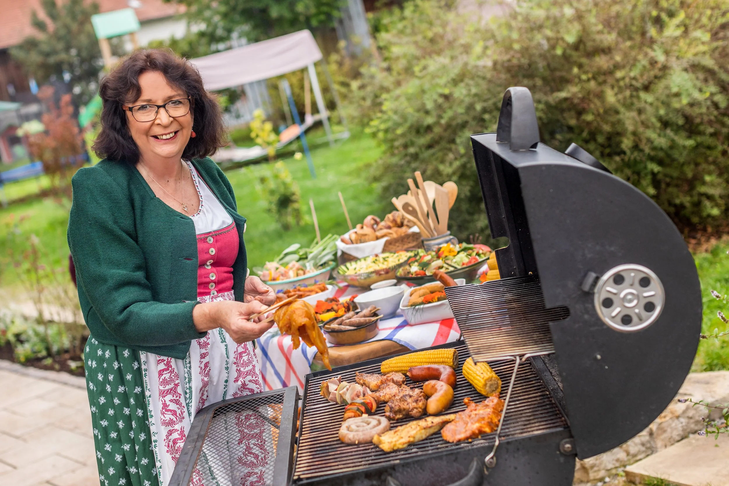Eine fröhliche Frau beim Grillen im Garten, die verschiedene gegrillte Speisen und Beilagen genießt.