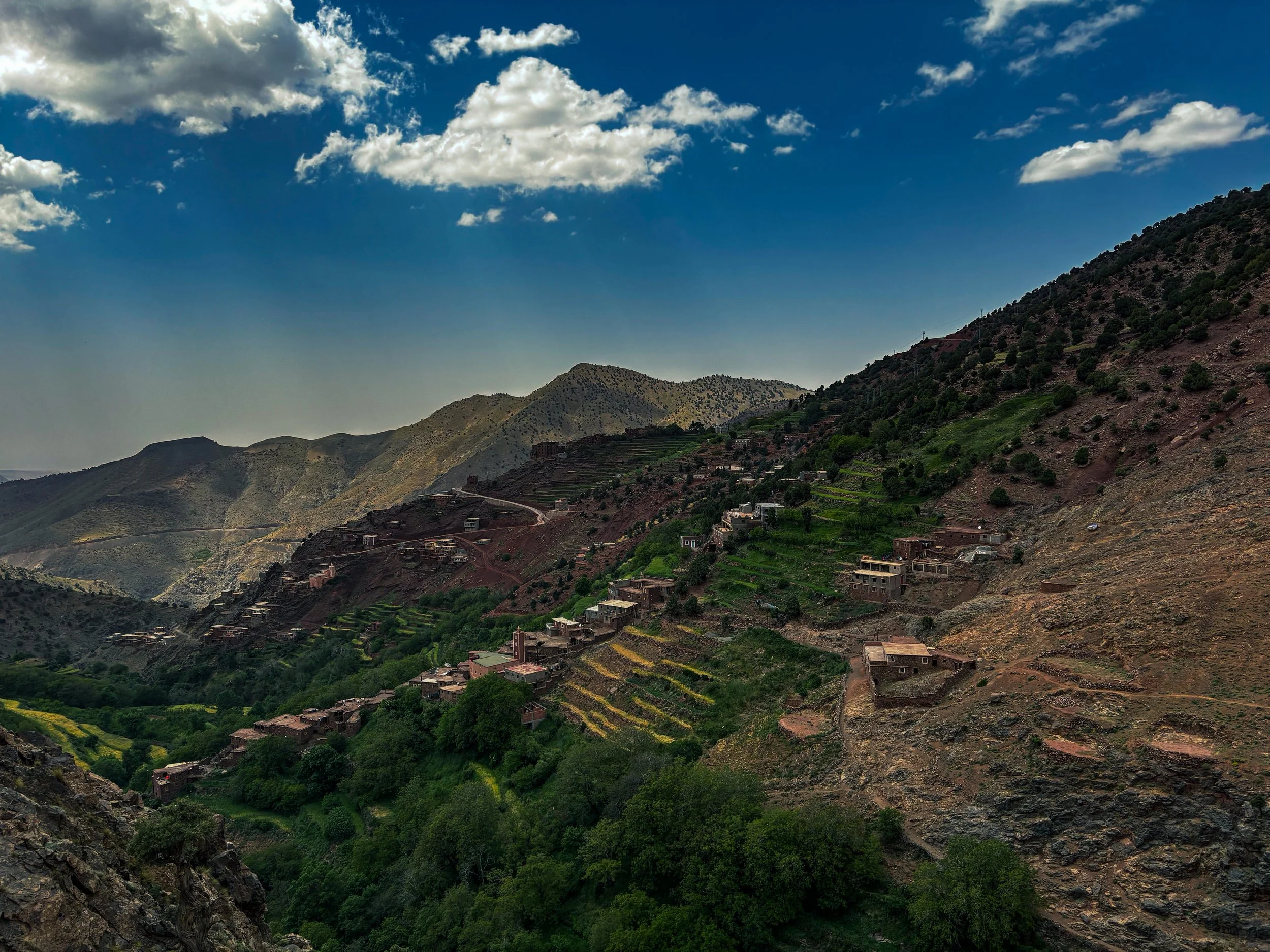 Scenic view of a mountainous region with terraced fields and small houses, under a partly cloudy sky.