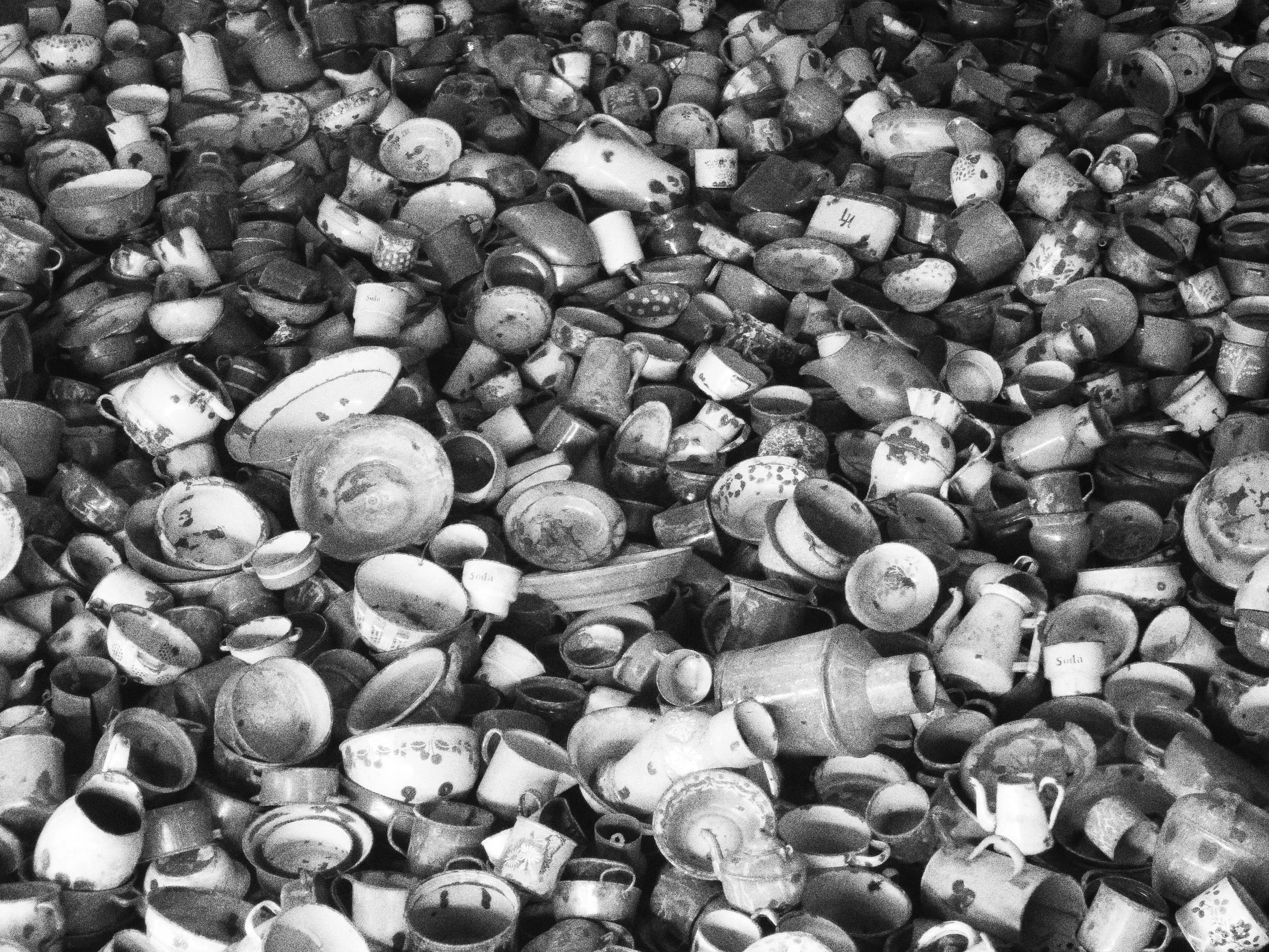 A large pile of broken and intact ceramic cups and mugs, many with visible decorative patterns, piled high in black and white.