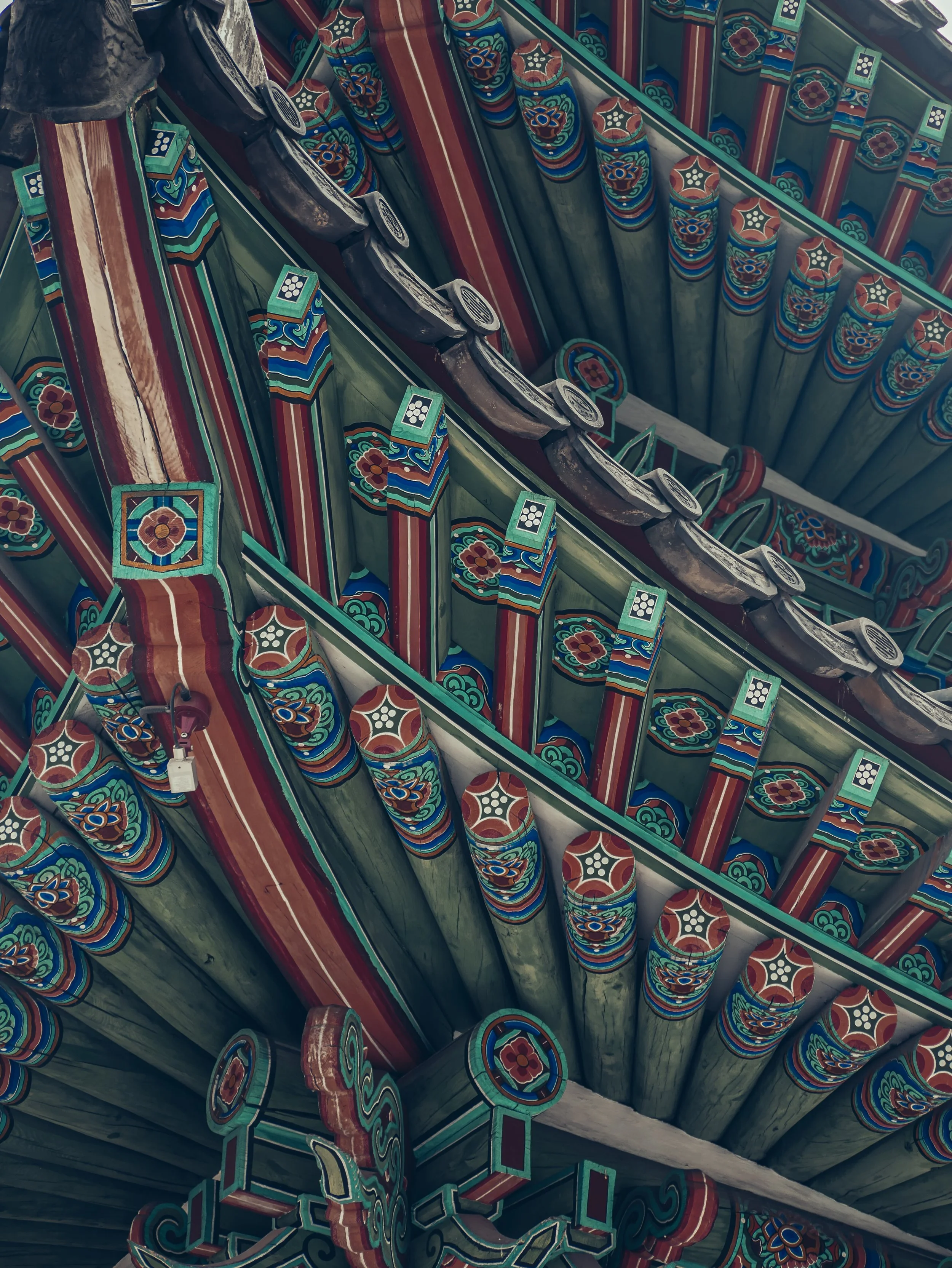Close-up of traditional Korean architectural detailing, showing colorful, ornate wooden brackets and beams with floral and geometric patterns in red, green, blue, and black.