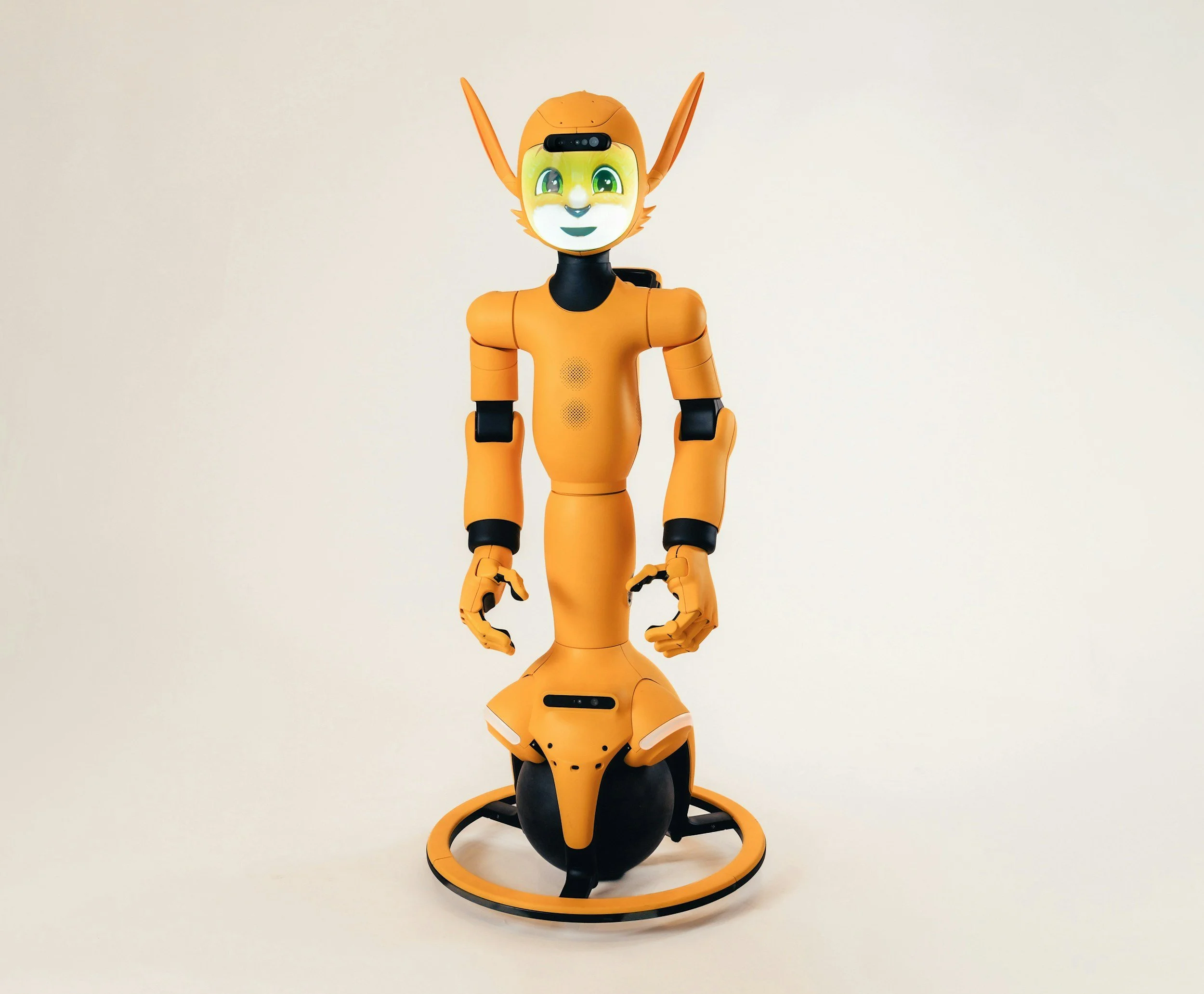 A humanoid robot with an orange body and black limbs, standing against a plain white background. The robot has a friendly, smiling face with green eyes and a digital display.