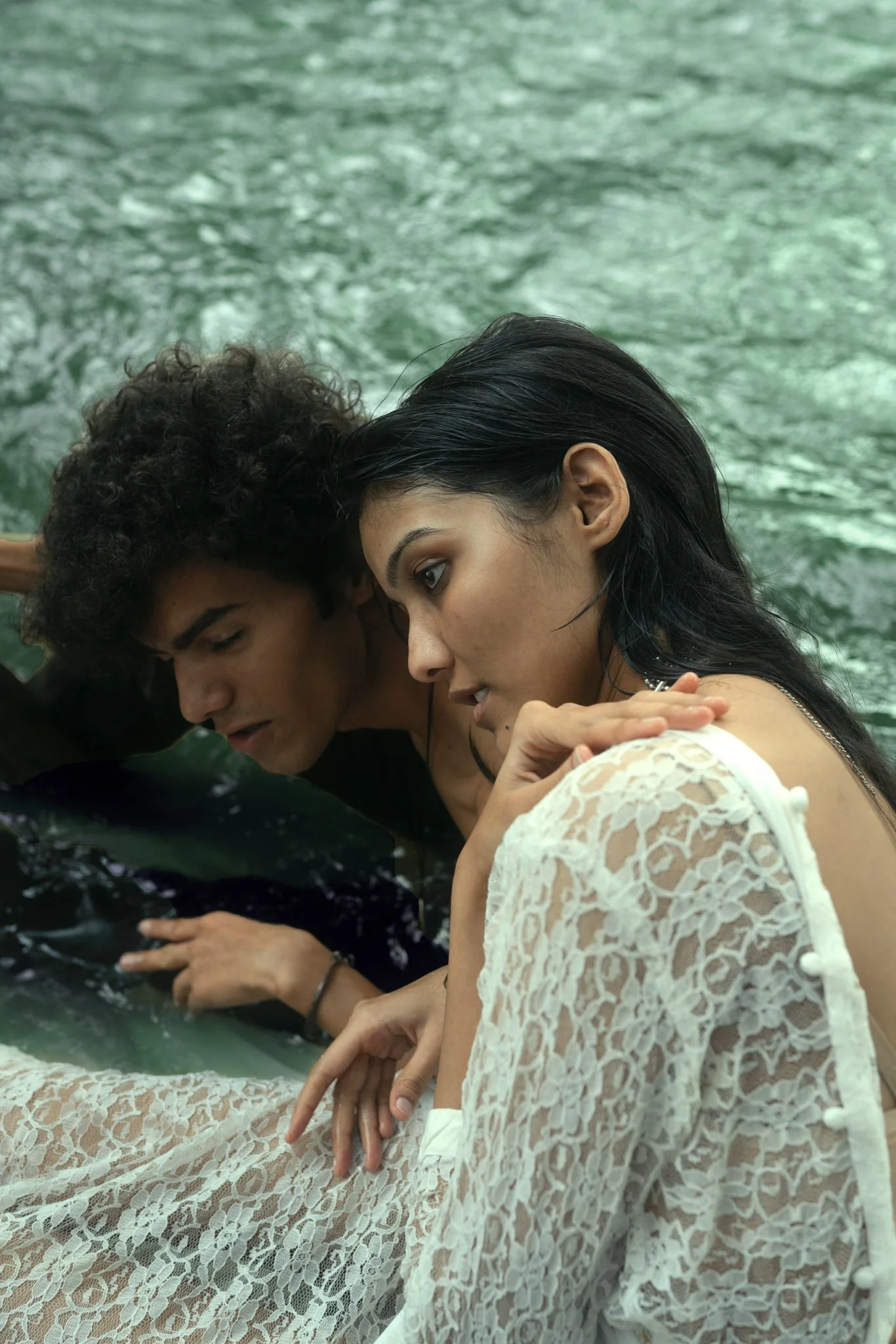 A man and woman leaning over the edge of a boat, looking at the water below, with a greenish water background.