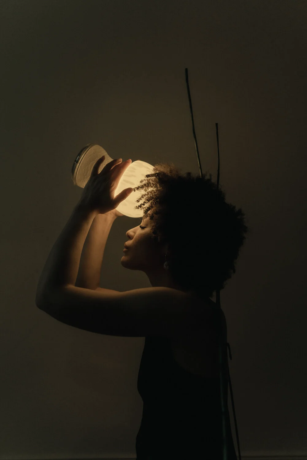 A woman with natural curly hair is holding a bright light fixture close to her face in a dark room