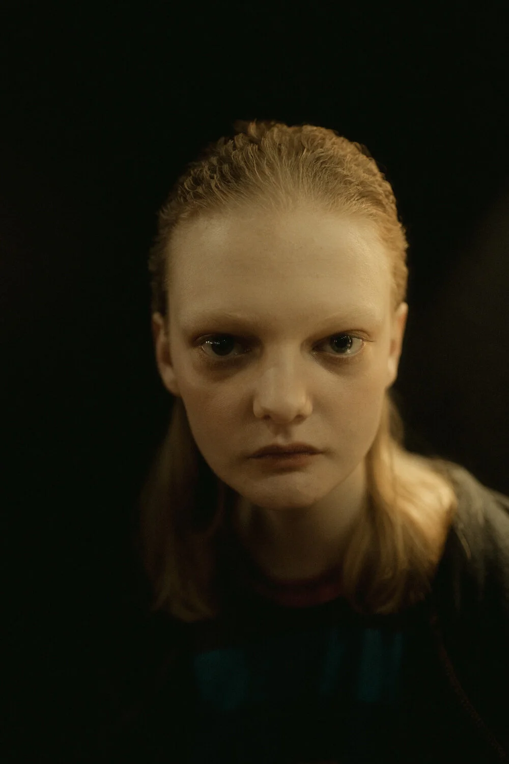Close-up portrait of a woman with wet, slicked-back hair, pale skin, and intense expression against a dark background