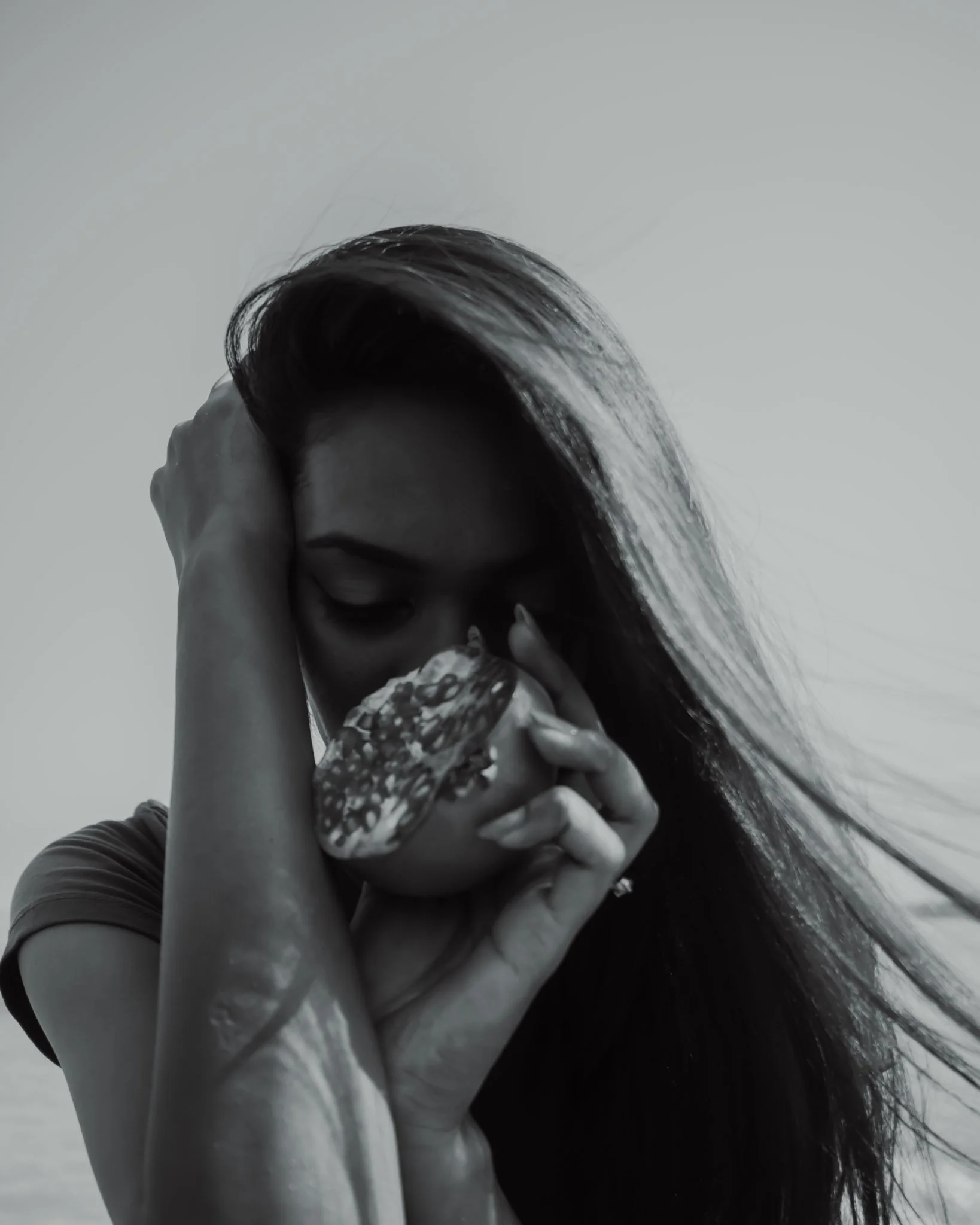 A black and white photo of a woman with long hair covering part of her face, hand on her head, holding a butterfly near her face.