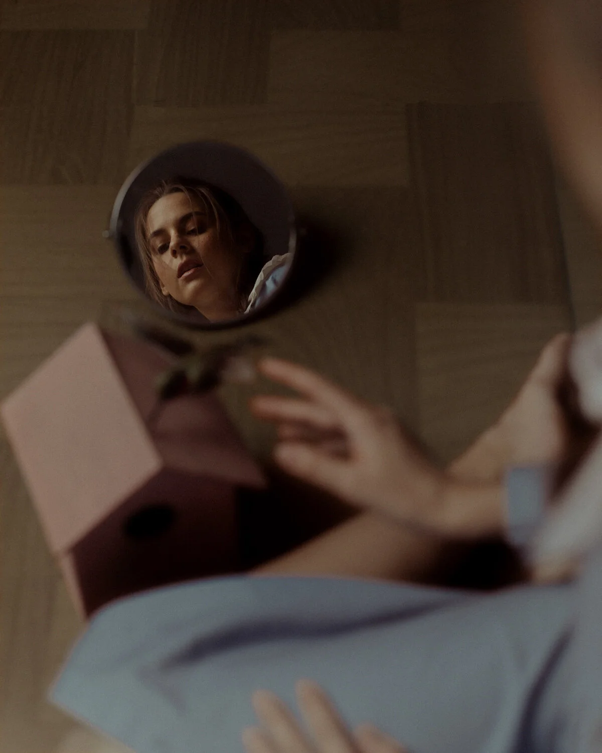 A woman looking at herself in a small round mirror placed on a table, seen from above.