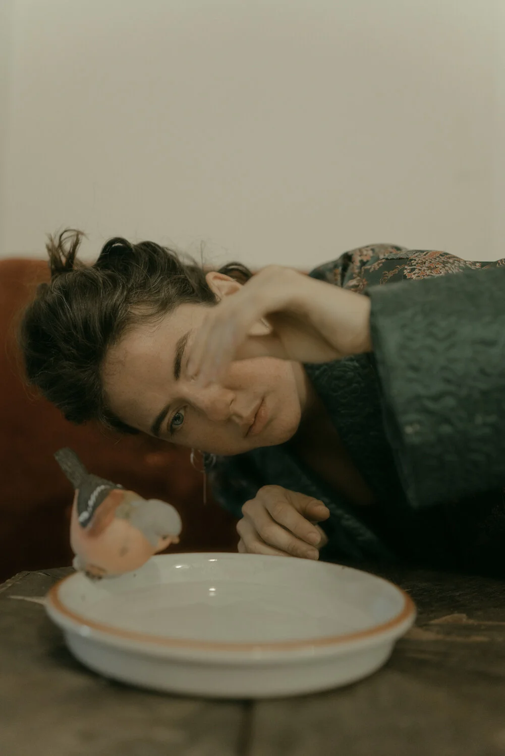Person with short dark hair and light skin leaning over a wooden table, holding a spoon and about to eat from a white bowl, with a neutral expression.