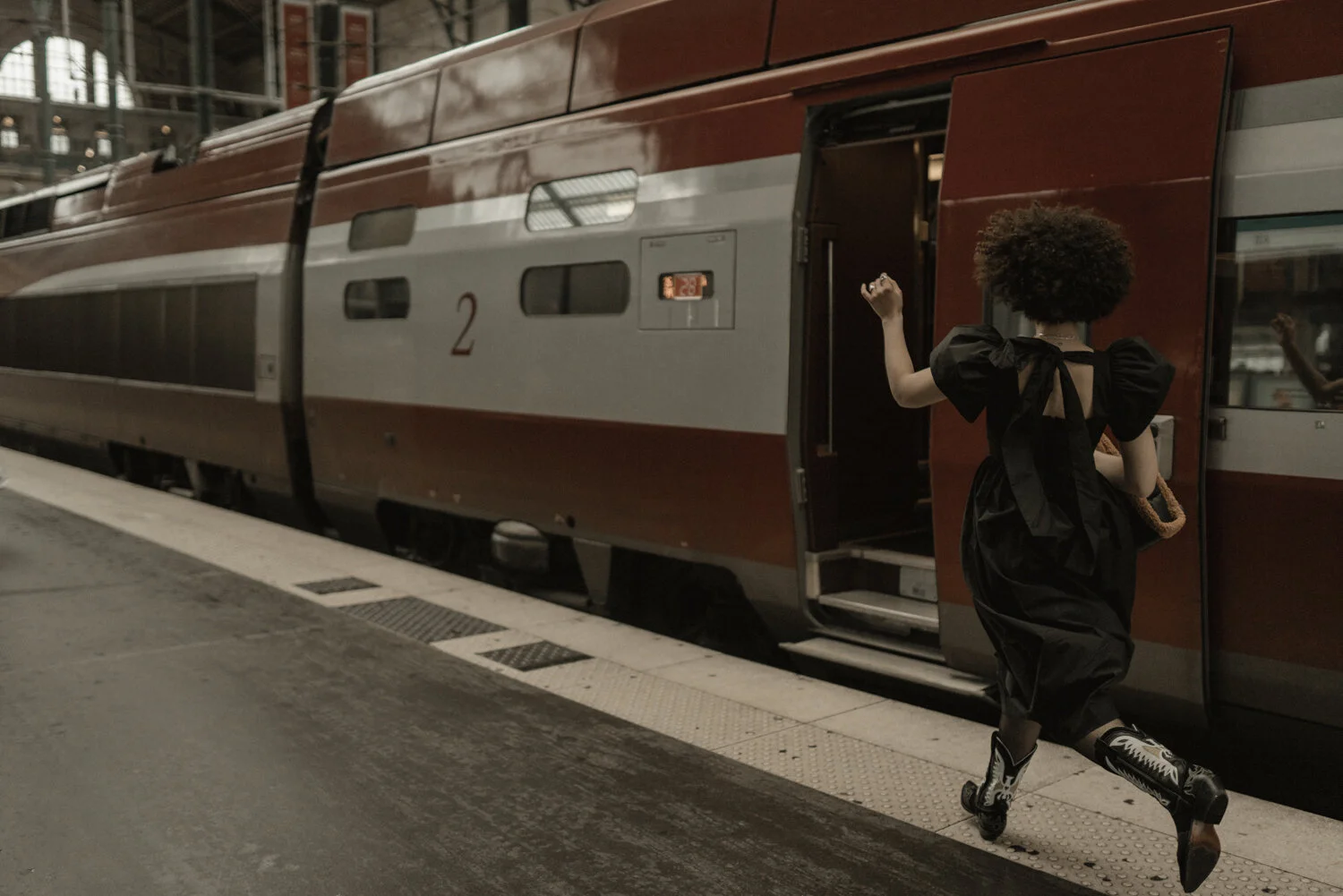 A woman with curly hair dressed in a black outfit running to catch a train at a station.