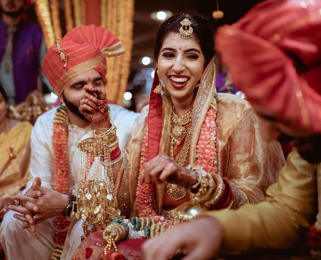 Indian bride and groom during a wedding ceremony, dressed in traditional attire, joyful and exchanging smiles.