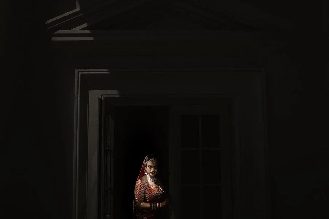A woman dressed in traditional Indian bridal attire standing in the doorway of a dark room.