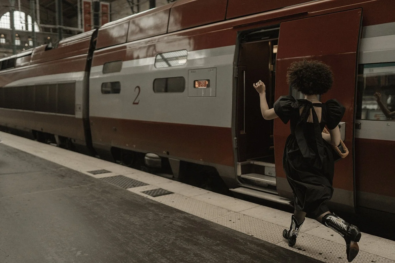 A woman with curly hair wearing a black dress and rollerblades stepping onto a train at a station.
Shot by Shetty Karthik