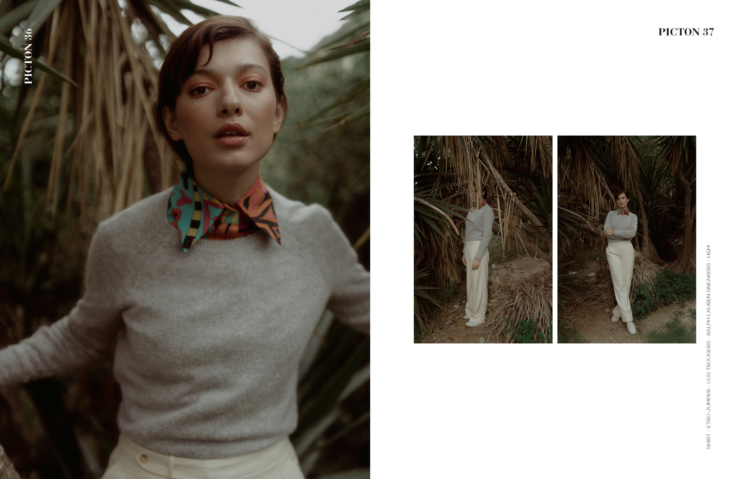 A woman with short hair wearing a gray sweater, colorful patterned neckerchief, and cream-colored trousers standing outdoors among trees and foliage.