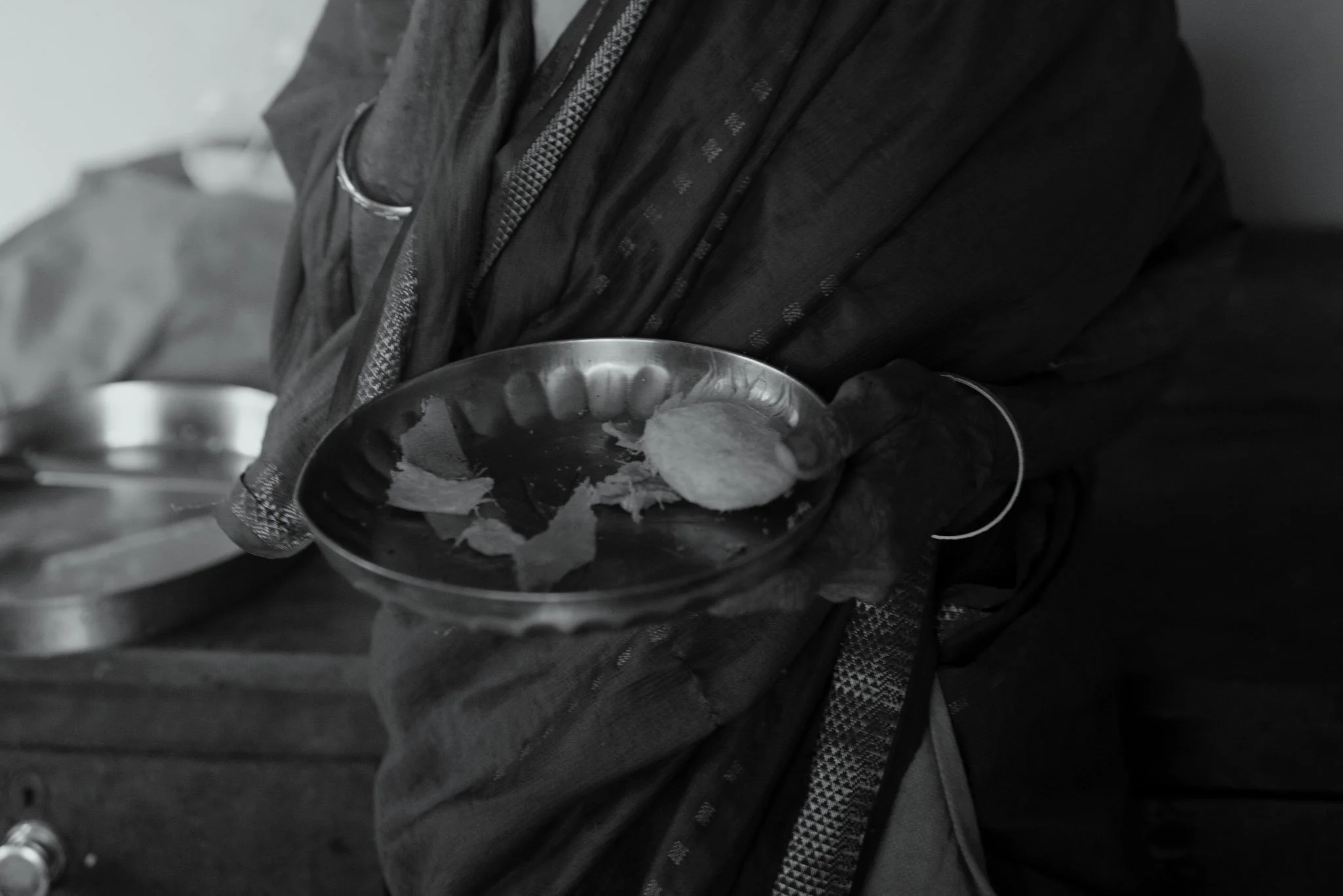 A person wearing black gloves holding a small metal bowl with slices of bread inside.