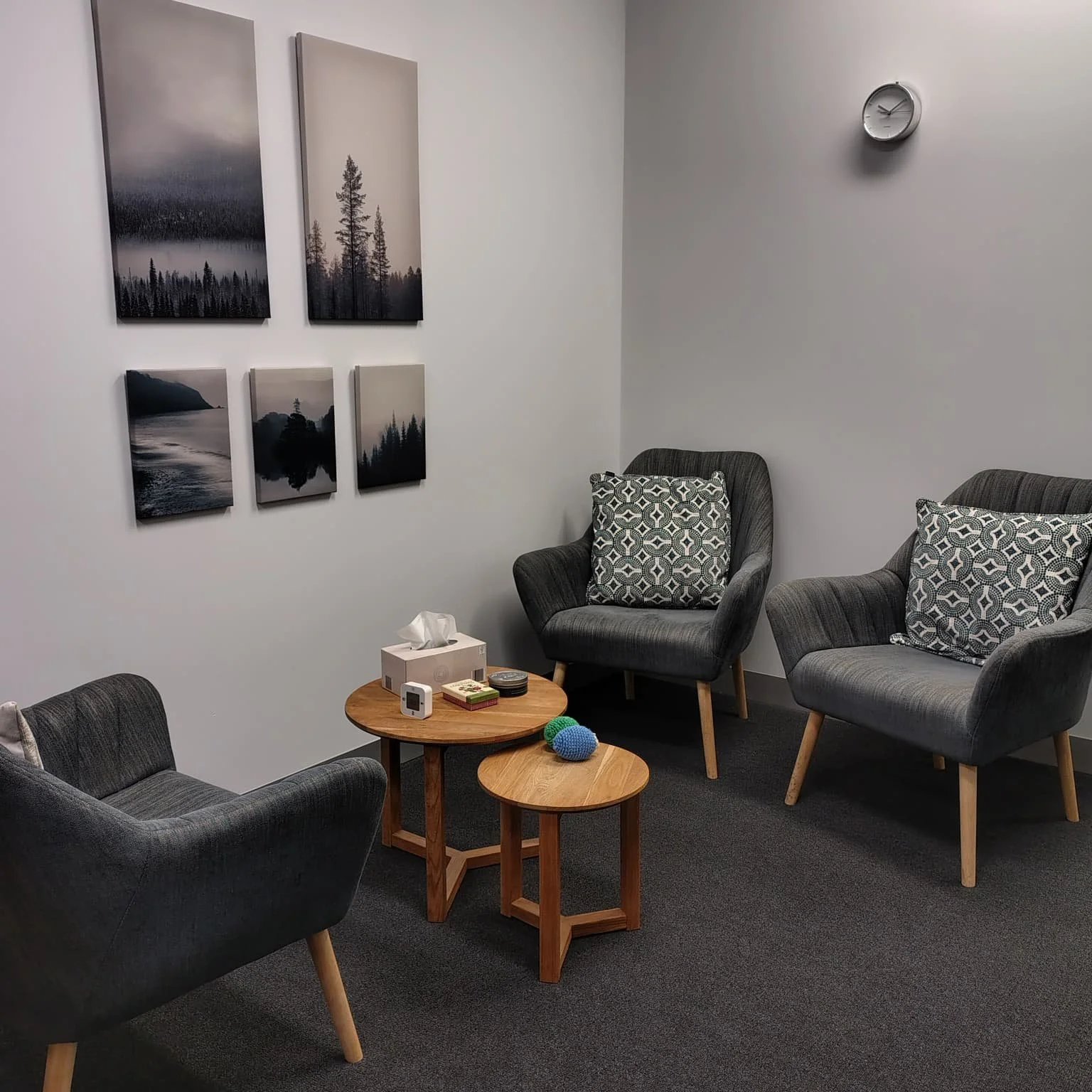 A small room with gray armchairs, a round wooden table with some items, and three black-and-white landscape paintings on the wall.