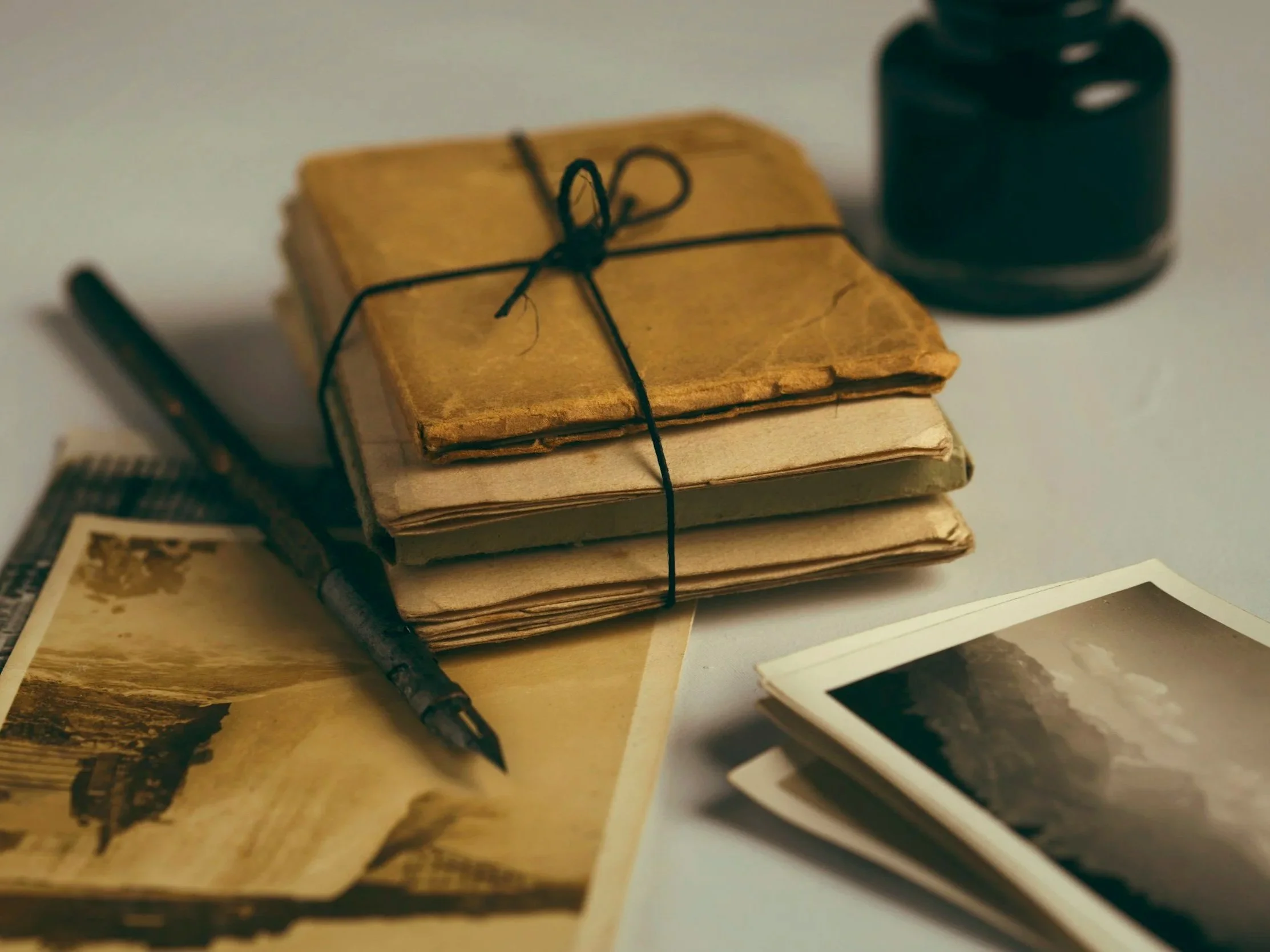 a package of documents tied together with string, with a dip pen and ink pot to the side and some old photographs