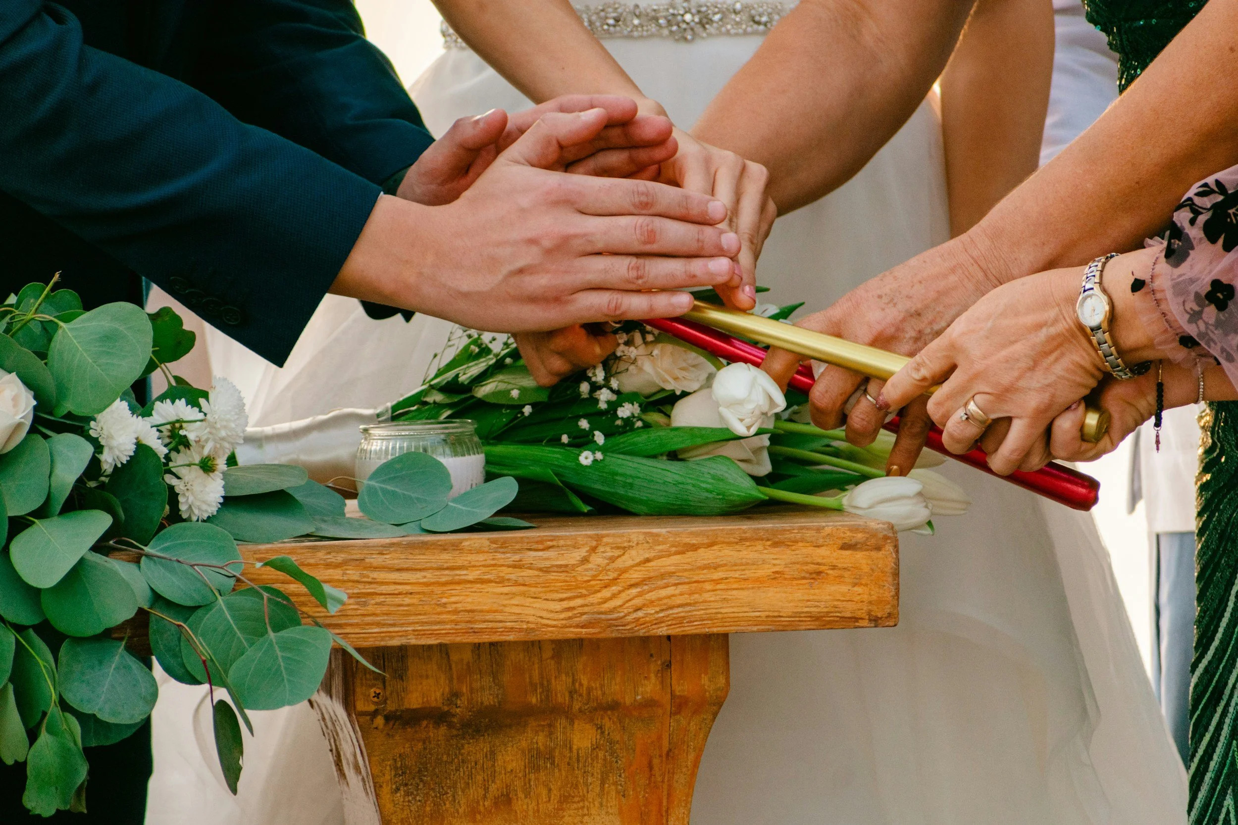many hands lighting candles together over a bouquet of flowers on a table at a wedding