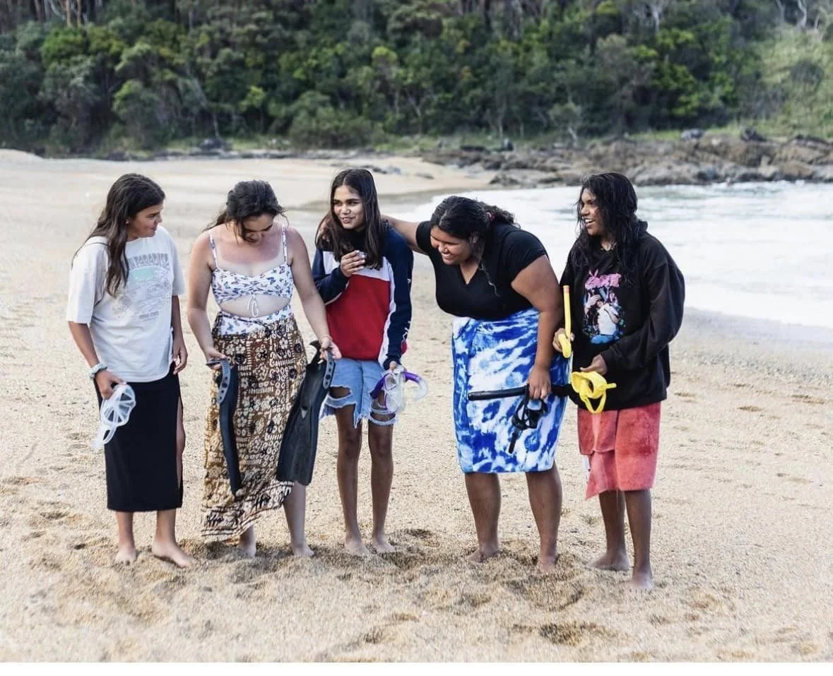 Group of women standing on the beach, smiling and talking, with snorkeling gear in their hands.