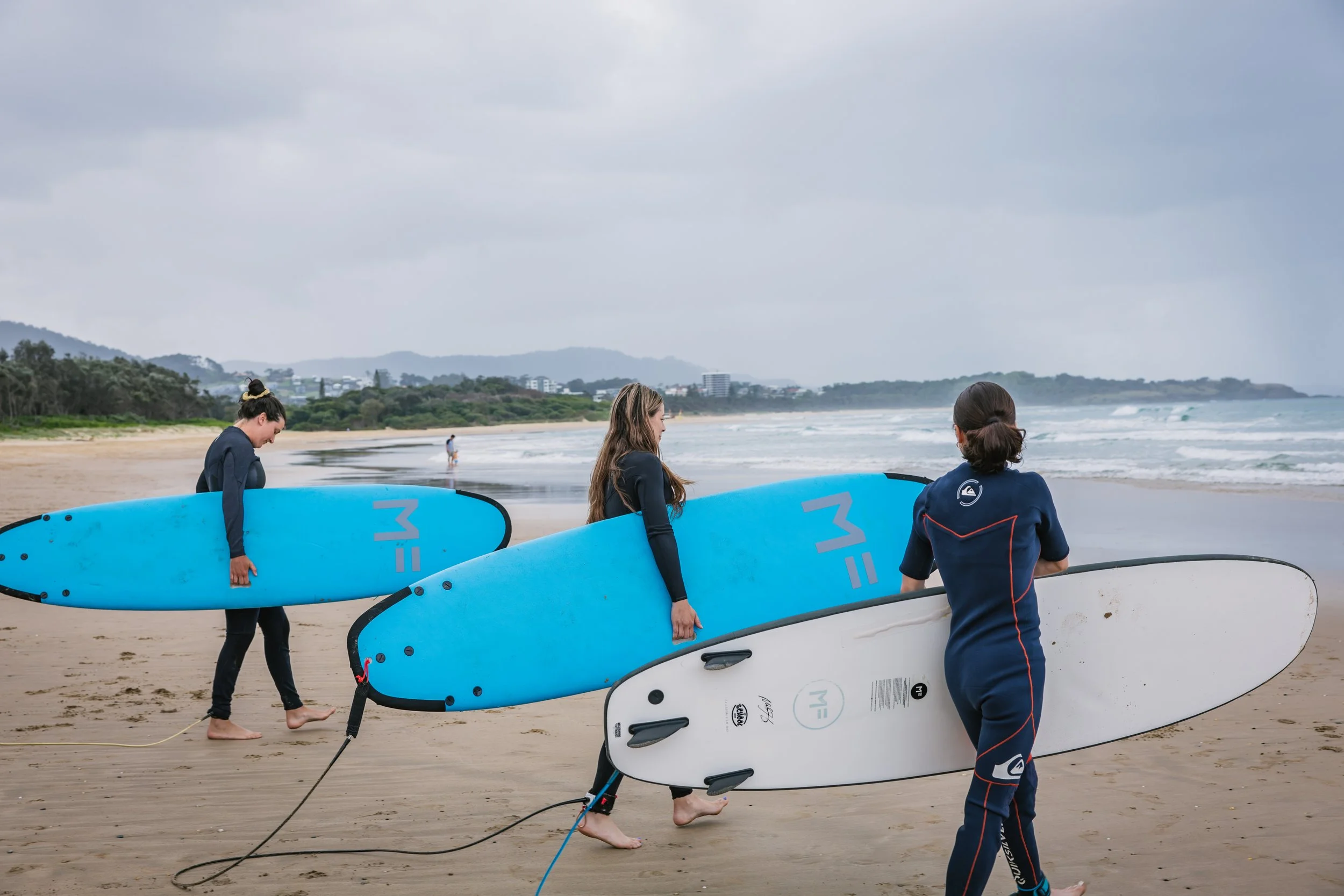 People carrying surfboards on a cloudy beach.