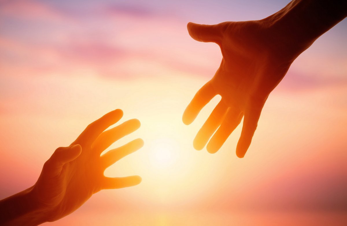Two hands reaching toward each other with sunset sky in the background.