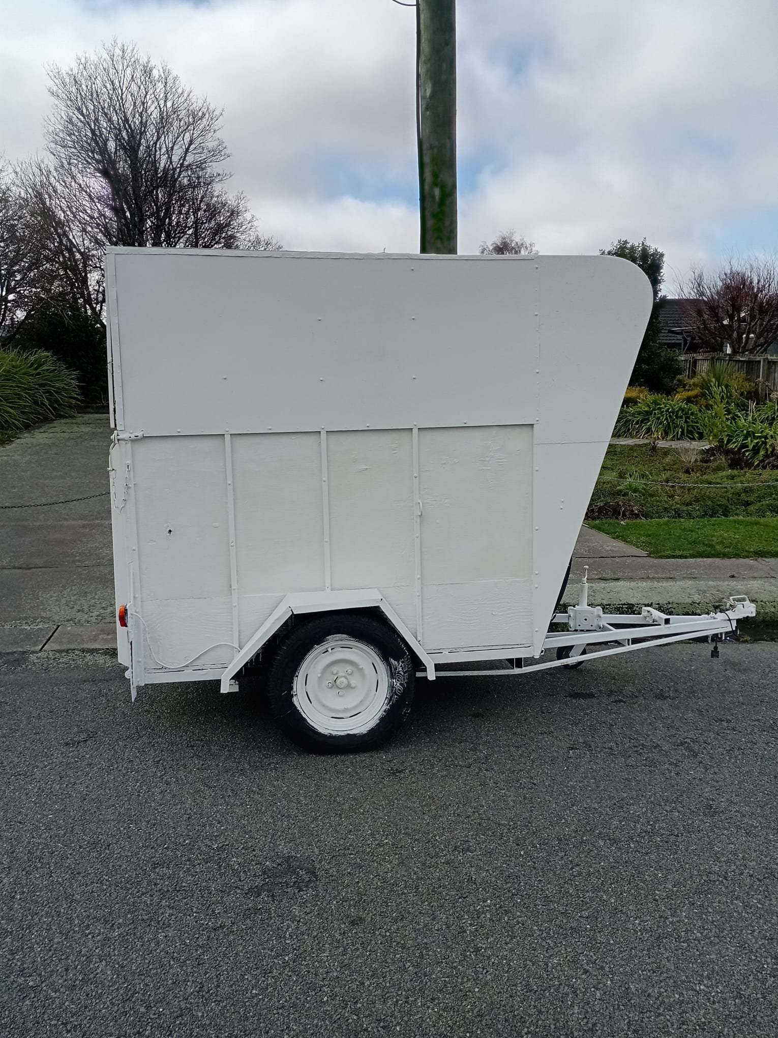 Empty white trailer parked on a paved surface with trees and cloudy sky in the background.