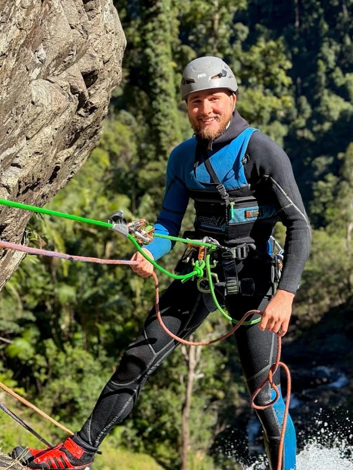 Canyoning guide wearing a helmet and harness beside a rock wall.