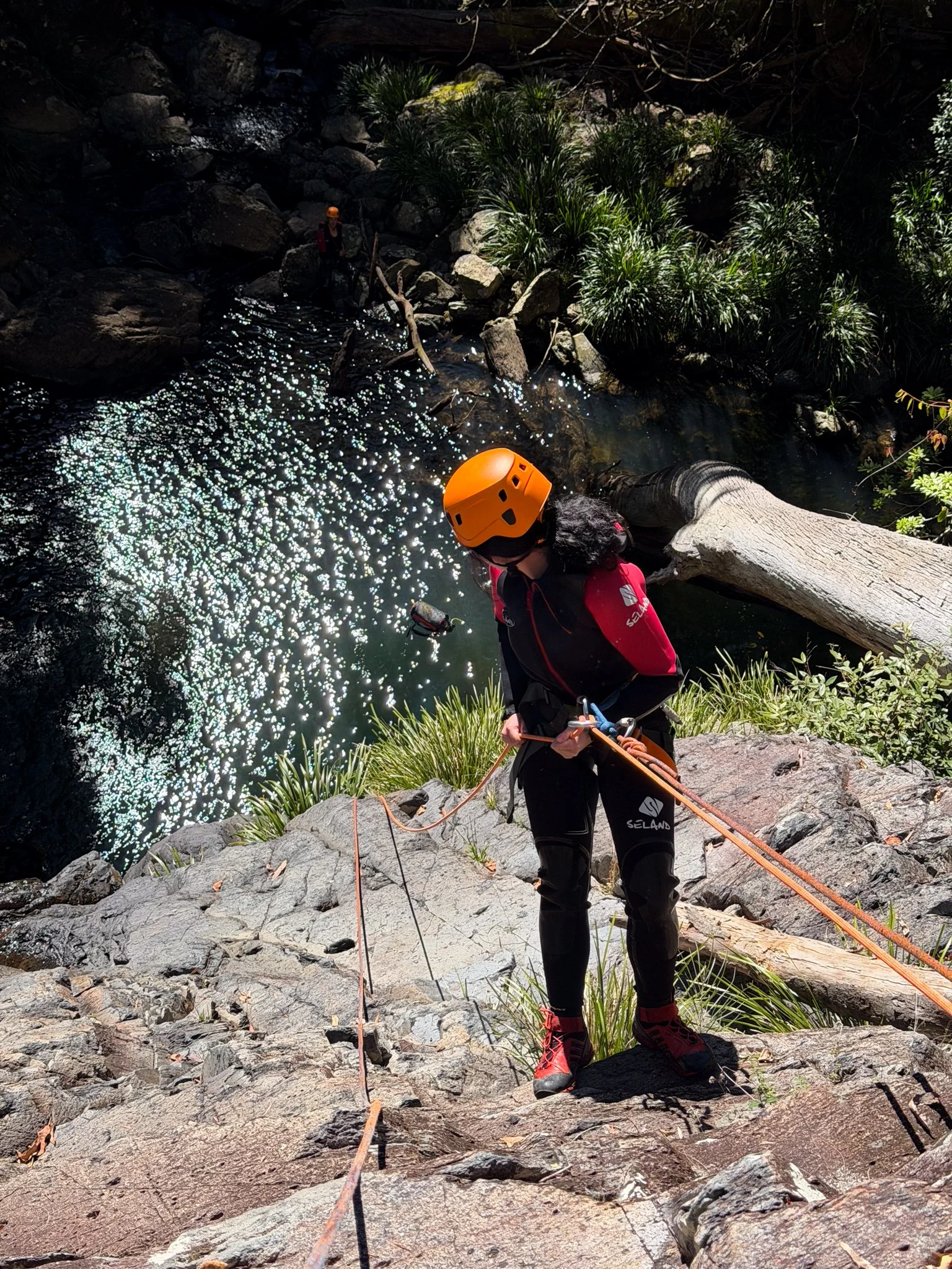 Canyoner in a helmet and harness preparing beside a rope above a canyon pool.