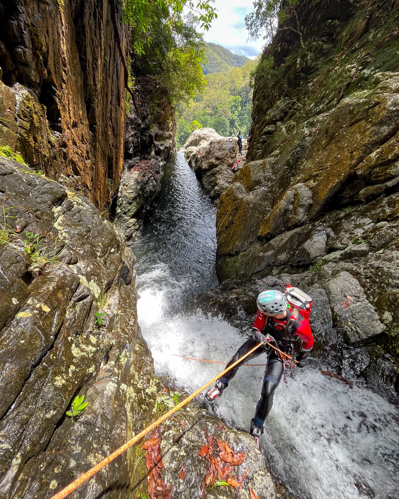 Canyoner abseiling on a rope beside a waterfall in a narrow gorge.